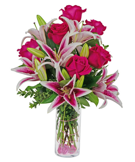 Stargazer lilies and roses are arranged in a cylinder vase with stones, wire and more. 