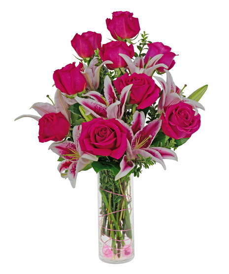 Stargazer lilies and roses are arranged in a cylinder vase with stones, wire and more. 