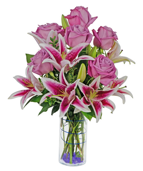 Stargazer lilies and roses are arranged in a cylinder vase with stones, wire and more. 