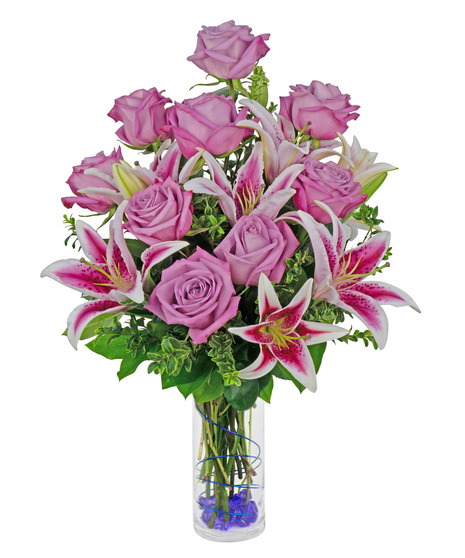 Stargazer lilies and roses are arranged in a cylinder vase with stones, wire and more. 