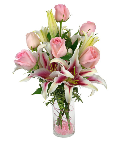 Stargazer lilies and roses are arranged in a cylinder vase with stones, wire and more. 