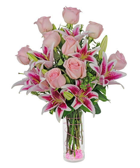 Stargazer lilies and roses are arranged in a cylinder vase with stones, wire and more. 