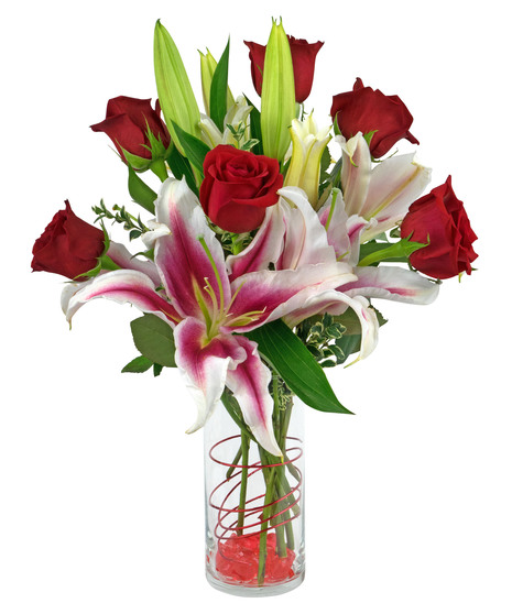 Stargazer lilies and roses are arranged in a cylinder vase with stones, wire and more. 