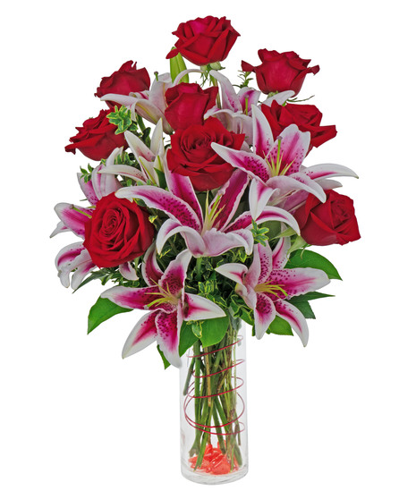 Stargazer lilies and roses are arranged in a cylinder vase with stones, wire and more. 